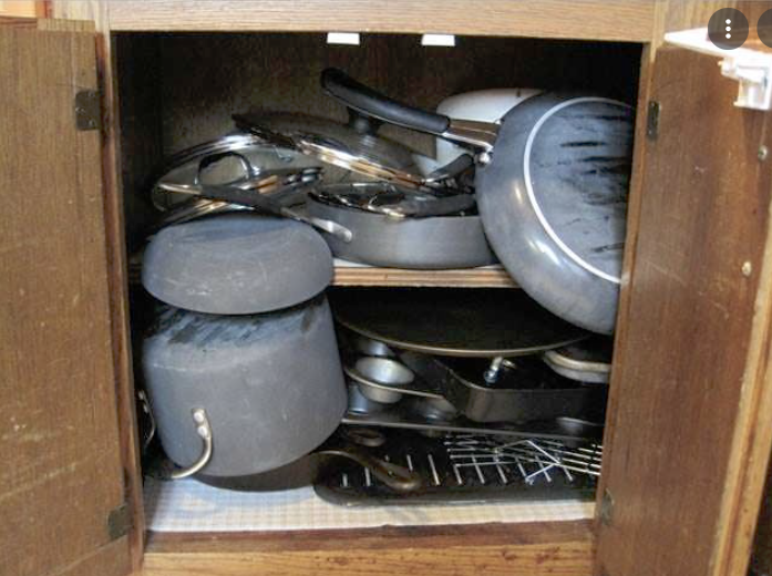 messy kitchen cabinet with pots on the top of each other